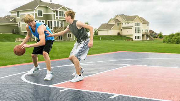 Two teenage boys are playing basketball on their home basketball court.