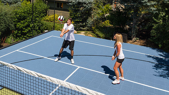 Two friends play volleyball on their backyard volleyball court.
